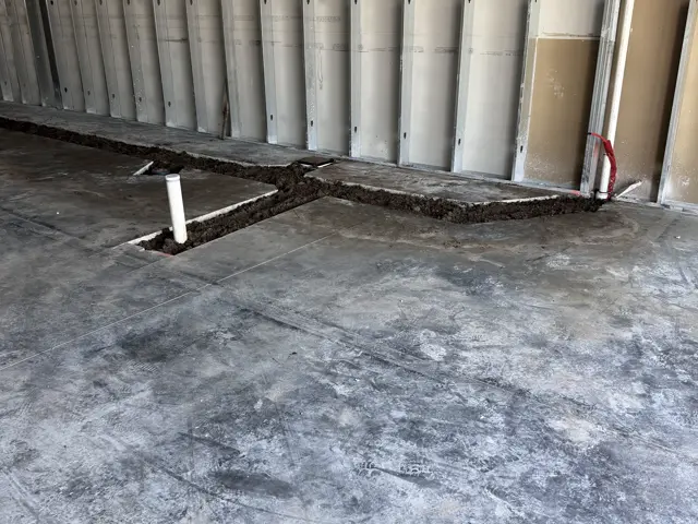 Saw-cut trench opened across an interior concrete slab with plumbing stub-ups in place