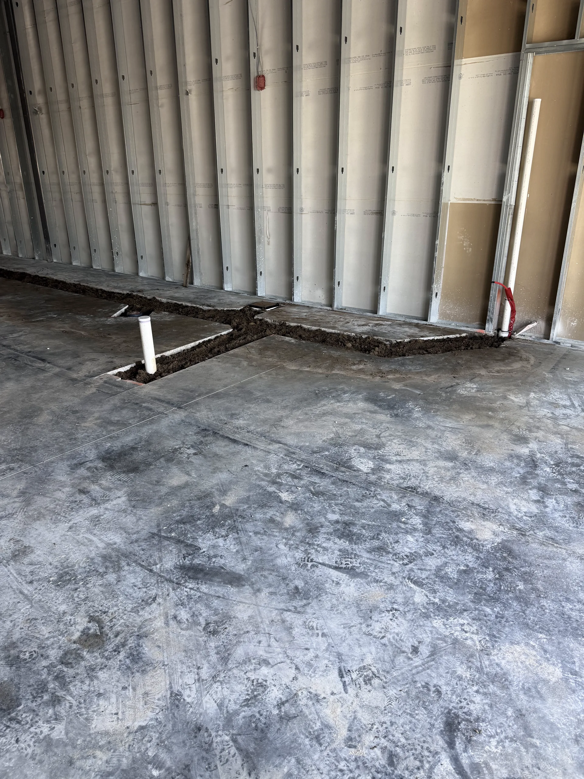 Saw-cut trench backfilled across an interior concrete slab with plumbing stub-ups in place