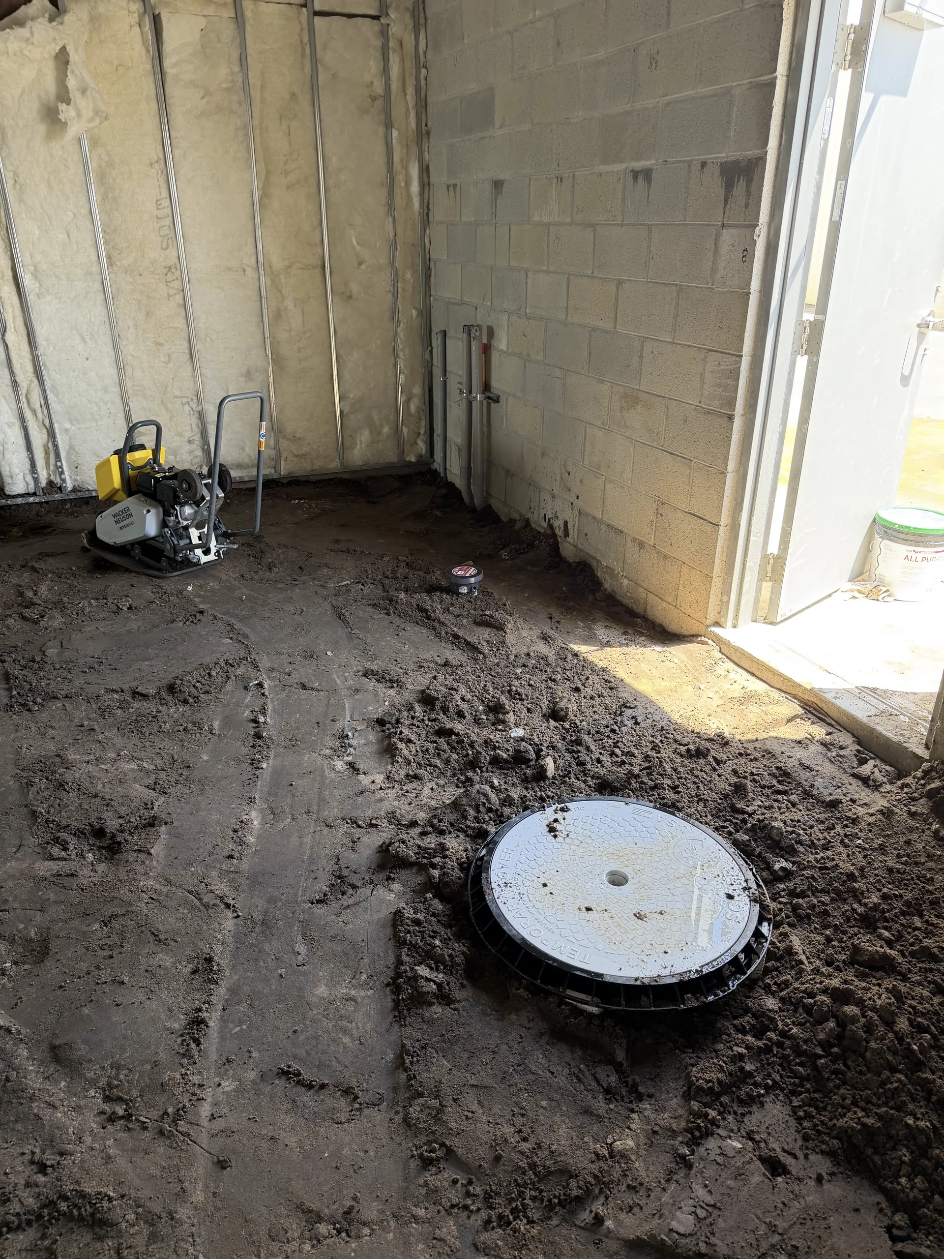 Trench backfilled and compacted around a set cleanout cover on a commercial interior job